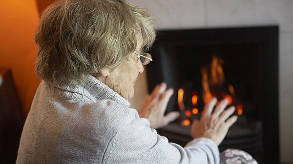 An elderly lady warming herself up with a fire.