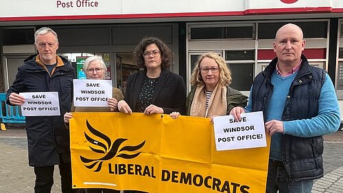 Cllrs and a member of the public outside windsor post office with a banner.